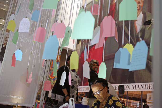 South African born Janita Lange, center bottom, writes her personal messages to former South African President Nelson Mandela, forming part of a exhibit on the former president in Cape Town, South Africa, Wednesday, Nov. 27, 2013. (AP Photo/Schalk van Zuydam)