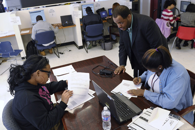 Akira Lee, front right and Scheryl Duarte, left, both seniors at Roosevelt High School, talk with Martin Copeland, the school's DC College Access Program adviser, as they fill out a college enrollment application at the school in Washington, Nov. 14, 2013. (AP Photo/Susan Walsh)  