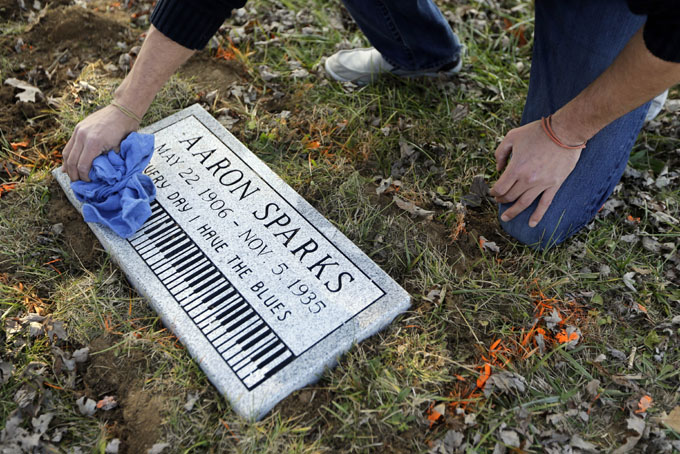 In this photo made Wednesday, Dec. 4, 2013, Aaron Pritchard wipes off a headstone after laying the marker on the previously unmarked grave of blues musician Aaron Sparks in Crestwood, Mo. Pritchard is part of the Killer Blues Headstone Project, a nonprofit effort to posthumously honor sometimes long-forgotten blues musicians with grave markers. The group has laid 22 headstones to date, with several more complete but awaiting placement. (AP Photo/Jeff Roberson)