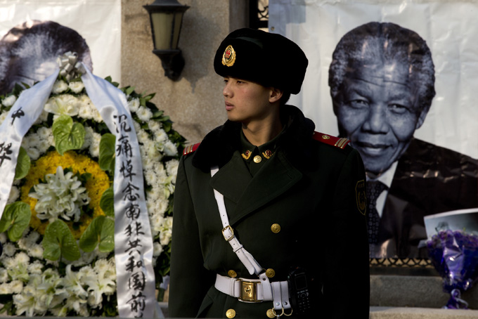 A Chinese paramilitary policeman stands guard near a wreath of flowers and a portrait of former South African President Nelson Mandela displayed outside the South African Embassy in Beijing, Friday, Dec. 6, 2013. South Africa's President Jacob Zuma said Mandela has died at age 95. (AP Photo/Andy Wong)