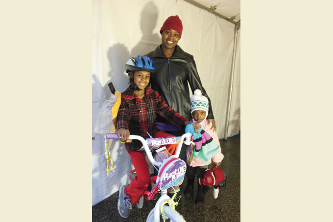 LET’S RIDE—Tiffany Dotson, of Garfield, with her daughters, Taylor Dotson, 9, left, and Sienna Dotson, 3. Taylor sits on the bike she received from Pittsburgh Bureau of Police during their annual Holiday Bike Giveaway held on Dec. 21 at the Zone 5 Police Station. (Photo by J.L. Martello)