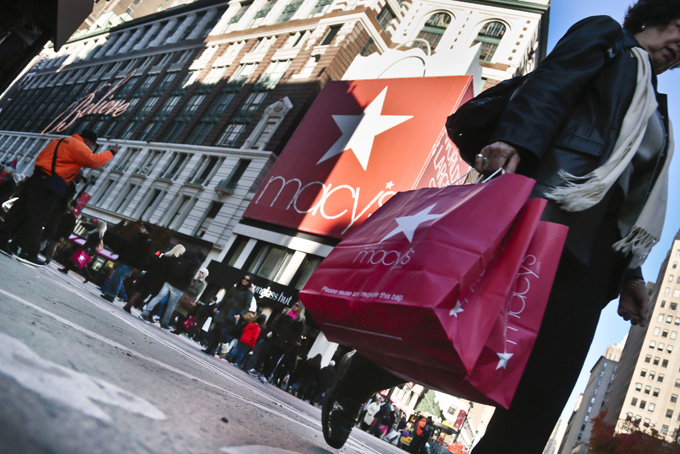 This Nov. 23, 2013 file photo shows a shopper carries Macy's bags while crossing an intersection outside Macy's in New York. Getting up early on Cyber Monday for a little shopping? It’s all in the name of gift-giving _ or at least the guise of it. It seems a lot of consumers are using these sales and retail events to treat themselves to a new little something. (AP Photo/Bebeto Matthews, File)