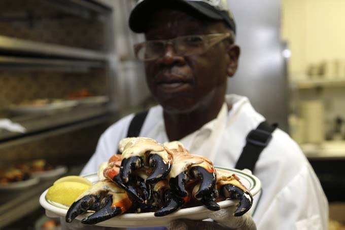 In this Tuesday, Oct. 22, 2013 photo, Eugene Green holds up a plate of stone crabs while working in the kitchen at Joe's Stone Crab restaurant in Miami Beach, Fla. Green has worked for the restaurant for over forty years. Joe's Stone Crab has been family-owned from the start when it opened in 1913 as a mom-and-pop fish house. Today, it’s a must-stop spot where wearing a bib over fine-dining attire is the norm. (AP Photo/Lynne Sladky)