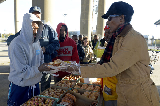 This Nov. 24, 2013 photo shows Yolanda Brandon, right, serving food to Ronnie Stewart on Sunday at the I-10 overpass in Baton Rouge, La. For three years, Fellowship Church in Prairieville has had a homeless ministry where they lead church services under the overpass. Each week, they hand out coats and serve food to between 75 and 150 people. (AP Photo/The Advocate, Catherine Threlkeld)