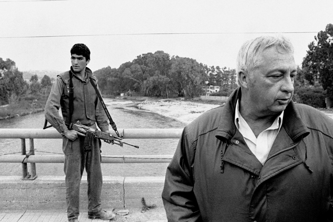 In this March 7, 1984 file photo, an Israeli soldier keeps his finger on the trigger of his assault rifle while Former Defense Minister Ariel Sharon, right, stands on the bridge overlooking the Awali River, Israel's most northerly position in Sidon, Lebanon. Sharon, the hard-charging Israeli general and prime minister who was admired and hated for his battlefield exploits and ambitions to reshape the Middle East, died Saturday, Jan. 11, 2014. The 85-year-old Sharon had been in a coma since a debilitating stroke eight years ago. (AP Photo/Max Nash, File)