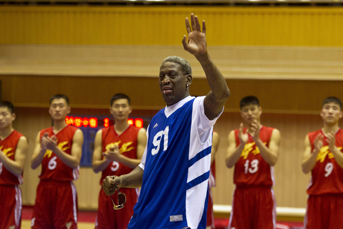 Dennis Rodman waves to North Korean leader Kim Jong Un, seated above in the stands, after singing Happy Birthday to Kim before an exhibition basketball game with U.S. and North Korean players at an indoor stadium in Pyongyang, North Korea on Wednesday, Jan. 8, 2014. (AP Photo/Kim Kwang Hyon)
