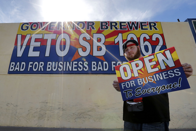 Josh Deinert, a graphic designer at Fast Signs, shows an anti-Senate Bill 1062 sign that reads "Open For Business To Everyone", Wednesday, Feb. 26, 2014 in Phoenix. Arizona Gov. Jan Brewer will hold a series of private meetings with opponents and proponents of legislation adding protections for people who assert their religious beliefs in refusing service to gays. Brewer spokesman Andrew Wilder says the governor will spend Wednesday gathering information about Senate Bill 1062 as she considers signing it into law or a veto. She has until Saturday to act. (AP Photo/Matt York)