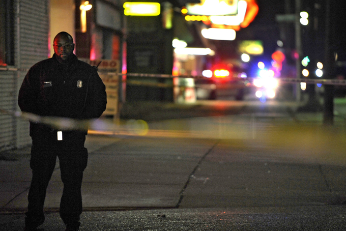In this Wednesday, Nov. 6, 2013 file photo, a Detroit Police officer stands guard behind barrier tape at the scene of a shooting which left three dead at a barbershop in Detroit. Police Chief James Craig points to a 14 percent decline in criminal homicides in 2013 from the previous year - from 386 in 2012 to 333 - precisely the same number of homicides that occurred in New York City, which has a population almost a dozen times larger than Detroit’s. (AP Photo/Detroit News, Elizabeth Conley)