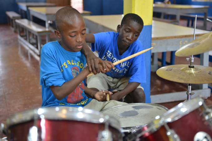 In this Feb. 17, 2014 photo, 14-year-old Brad Hylton helps classmate Omar Bird play a drum beat with the band at Alpha Boys’ School, a residential vocational school in Kingston, Jamaica. (AP Photo/David McFadden)