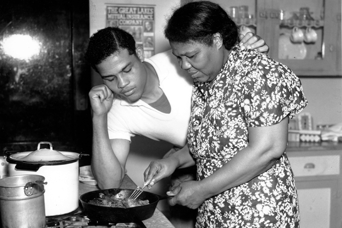 In this undated file photo, boxer Joe Louis watches his mother, Lila Brooks, fry chicken as he arrives home in Detroit, Mich. In mid-20th century America, at least on the surface, there seemed to be an overwhelming consensus of what manhood was all about. The feminist movement that emerged in the 1960s fractured this consensus and fueled significant, though gradual, changes in many Americans' perceptions of gender roles and stereotypes. (AP Photo)