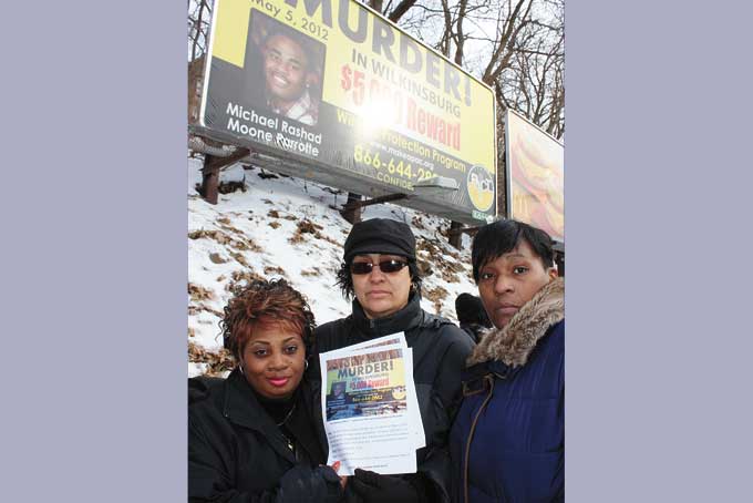 GOING AGAINST THE SILENCE—Tonya Moone, mother of Michael Rashad Moone Parrotte, who was killed in May 2012, stand with friends Toni Allen and Troi Baldwin in front of the Penn Avenue billboard, in Wilkinsburg. Moone is seeking information from witnesses for the conviction of her son's killer. (Photo by J.L. Martello)