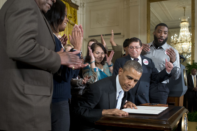 Surrounded by workers, President Barack Obama gets up from his chair after signing an executive order to raise the minimum wage for federal contract workers during a ceremony in the East Room of the White House in Washington, Wednesday, Feb. 12, 2014. Wage increase to $10.10 an hour, goes into effect next year, and applies to new contracts and replacements for expiring contracts. (AP Photo/Pablo Martinez Monsivais)