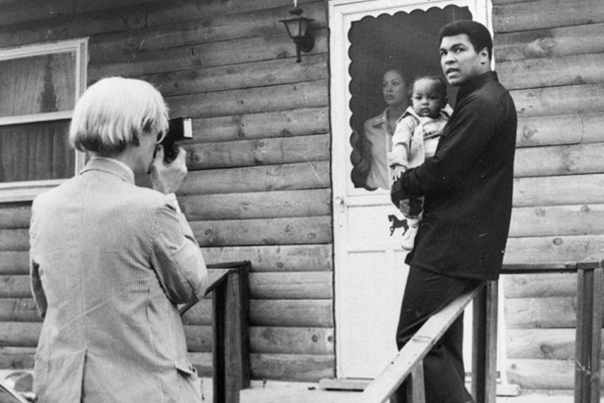 In this Thursday, Aug. 18, 1977 file photo, artist Andy Warhol, left, photographs Muhammad Ali, his infant daughter, Hanna, and wife, Veronica, at Ali's training camp in Deer Lake, Pa. (AP Photo)