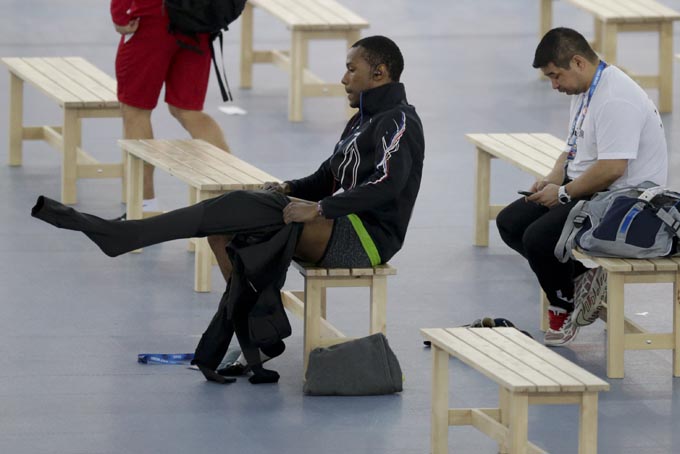 Shani Davis of the U.S., center, puts on the prototype of the official US Speedskating suit, while coach Ryan Shimabukuro checks his phone prior to a training session at the Adler Arena Skating Center at the 2014 Winter Olympics, Friday, Feb. 14, 2014, in Sochi, Russia. (AP Photo/Matt Dunham)