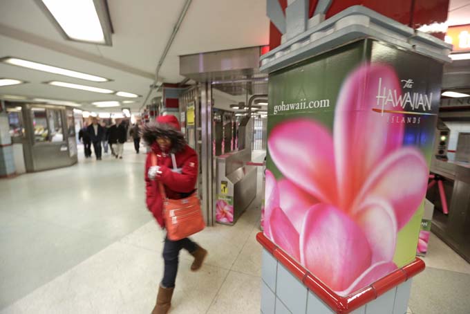 In this Wednesday, Feb. 26, 2014 photo, bundled up commuters walk past an advertisement for the Hawaiian Islands near a train stop in Chicago. (AP Photo/M. Spencer Green)
