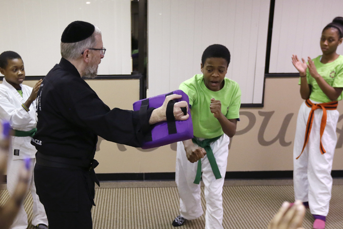 In a photo from Jan. 28, 2015 in Southfield, Mich., Da’Sean Williams, center, punches a strike pad held by Rabbi Elimelech Goldberg as Daunte Davis, left, and Jania Jordan, right, look on.  (AP Photo/Carlos Osorio)