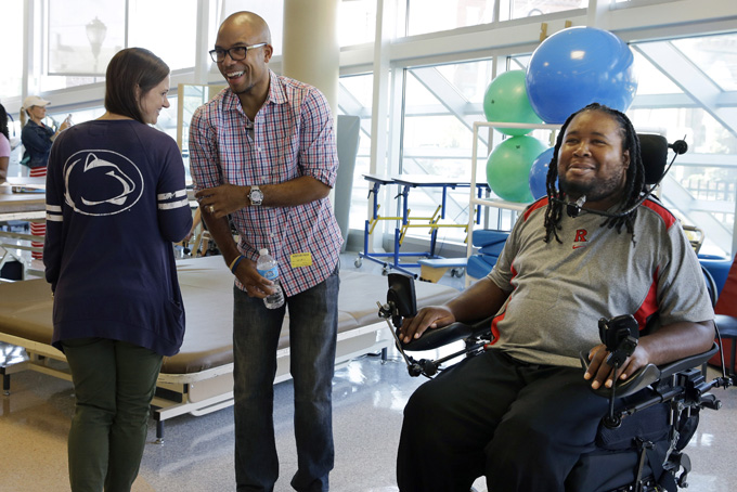 In this Wednesday, Sept. 10, 2014 file photo, Eric LeGrand, right, alumni of Rutgers University and Adam Taliaferro, center, alumni of Penn State University, both college football players who suffered serious spinal cord injuries on the field, react as child life specialist Tara Mohamed shows her Penn State shirt while visiting children at PSE&G Children's Specialized Hospital in New Brunswick, N.J. Taliaferro is a newly minted New Jersey state lawmaker. It is the latest step in a rapid rise up the public service ladder for a political neophyte who says he is motivated by helping others. (AP Photo/Mel Evans)