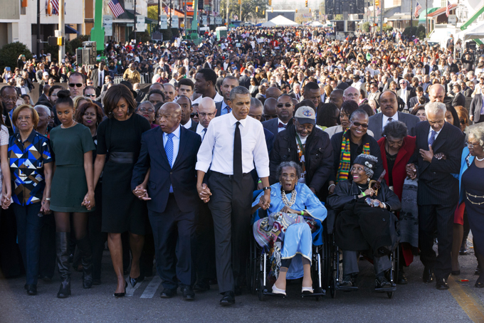 President Barack Obama, center, walks as he holds hands with Amelia Boynton Robinson, who was beaten during "Bloody Sunday," as they and the first family and others including Rep. John Lewis, D-Ga,, left of Obama, walk across the Edmund Pettus Bridge in Selma, Ala. for the 50th anniversary of “Bloody Sunday," a landmark event of the civil rights movement, Saturday, March 7, 2015. From front left are Marian Robinson, Sasha Obama. first lady Michelle Obama. Obama, Boynton and Adelaide Sanford, also in wheelchair. (AP Photo/Jacquelyn Martin)