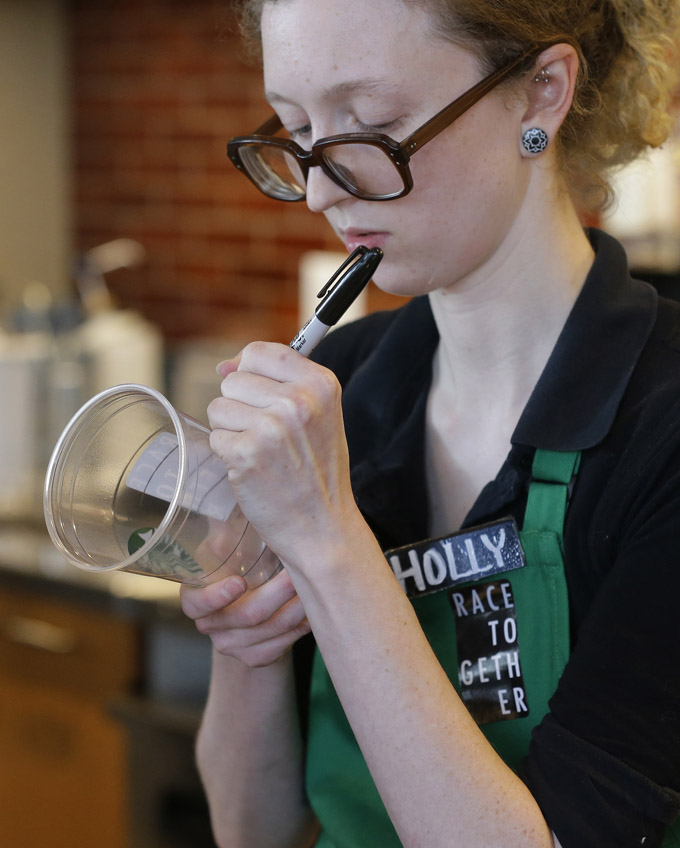 In a Wednesday, March 18, 2015 file photo, Holly Ainslie, a barista at a Starbucks store in Seattle writes on a cup for an iced drink as she wears a "Race Together" sticker. Starbucks baristas will no longer write "Race Together" on customers' cups starting Sunday, March 22, 2015, ending as planned a visible component of the company's diversity and racial inequality campaign, according to a memo. The coffee chain's initiative will continue more broadly without the handwritten messages, Starbucks spokesman Jim Olson said. (AP Photo/Ted S. Warren, File)