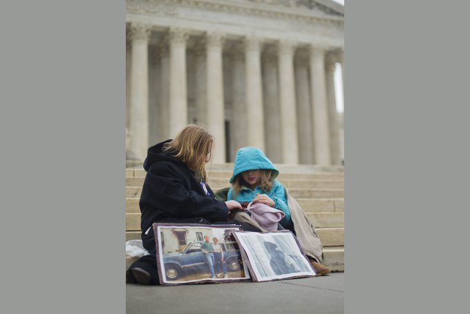 Helena Roberts, 11, left, and her sister Cassie Boyle, 8, from Pittsburgh, play with their dolls on the steps of the Supreme Court in Washington, Wednesday, March 4, 2015, as the court hears arguments in King v. Burwell, a major test of President Barack Obama's health overhaul which, if successful, could halt health care premium subsidies in all the states where the federal government runs the insurance marketplaces. The sisters are holding pictures of their grandmother Hannah Brown, who died when she was 58 years old. Their grandmother lost her job and healthcare and died a year and half later because of lack of access to treatment. (AP Photo/Pablo Martinez Monsivais)