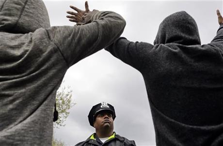 A member of the Baltimore Police Department stands guard outside of the department's Western District police station as men hold their hands up in protest during a march for Freddie Gray, Wednesday, April 22, 2015, in Baltimore. (AP Photo/Patrick Semansky)