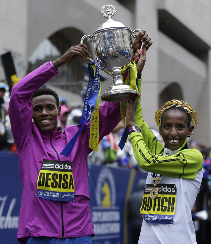 Boston Marathon winner Lelisa Desisa, left, of Ethiopia, and women's division winner Caroline Rotich, of Kenya, pose with a trophy, Monday, April 20, 2015, in Boston. (AP Photo/Elise Amendola)