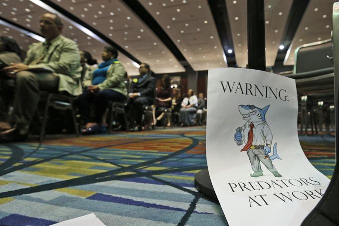 A sign warning of predatory payday lenders leans up against a chair during a speech by Consumer Financial Protection Bureau Director Richard Cordray, in Richmond, Va., Thursday, March 26, 2015. (AP Photo/Steve Helber)