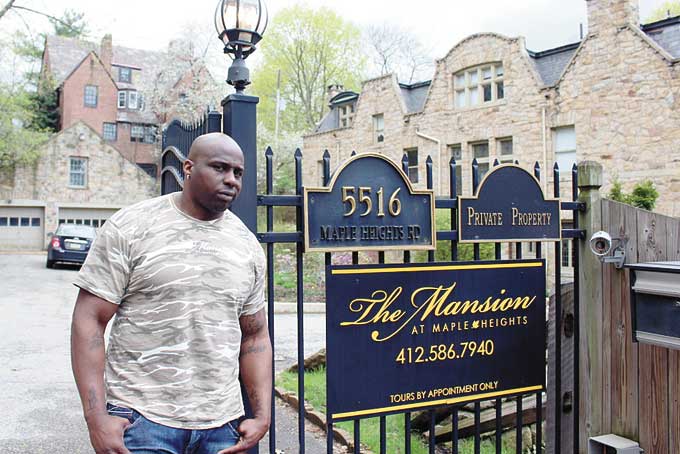 MANSION MISERY—Chukky Okobi stands by the gate to his Bed and Breakfast, which he says has been targeted via the courts by racist but well-connected neighbors who want drive him out.  