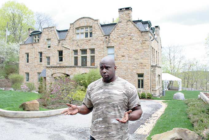 UPSET—Chukky Okobi outside his mansion. The tent, captured in the background, sits behind the house. (Photo by J.L. Martello) 