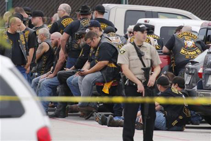 In this May 17, 2015 file photo, a McLennan County deputy stands guard near a group of bikers in the parking lot of a Twin Peaks restaurant in Waco, Texas. About 170 members of rival motorcycle gangs were charged with engaging in organized crime Monday, a day after a shootout at a Twin Peaks killed nine people and wounded 18. Some civil rights activists and media critics are wondering about the differences between public perceptions of the fatal violence in Waco, Texas, and protests in Baltimore and Ferguson, Missouri, over police killings of black men. (AP Photo/Jerry Larson) 