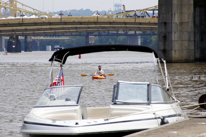 A kayaker floats behind a pleasure boat moored along the Allegheny River on the first day of the annual Three Rivers Regatta, Friday, July 3, 2015, in Pittsburgh. Officials announced earlier in a news conference that all water-based events, including the Formula One boat races, were canceled for the three-day festival because the rain-swollen rivers are unsafe. The concerts, the Fourth of July fireworks show, and other land-based events are still scheduled to go on. This year is the first in the event's 38-year history that all boating events have been canceled. The event normally draws about 500,000 people. (AP Photo/Keith Srakocic) 