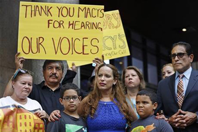 Vicente Mayorga, left, holds a sign next to Dominican immigrant Angela Lopez, front center, of Long Island, N.Y., as she stands with her sons Gabriel, left, and Adrian in front of Macy's Herald Square flagship store, Wednesday, July 1, 2015, in New York. Lopez and Mayorga joined other immigrants and politicians in calling on corporations and businesses to boycott presidential candidate Donald Trump after his remarks about Mexican immigrants. (AP Photo/Kathy Willens)