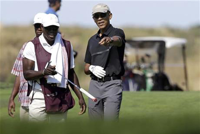 President Barack Obama, center, receives a club from a caddy, front left, while golfing at Vineyard Golf Club, in Edgartown, Mass., on the island of Martha's Vineyard, Monday, Aug. 10, 2015. The president is staying on Martha's Vineyard with first lady Michelle Obama and daughter Sasha for a 17-day island retreat. (AP Photo/Steven Senne)