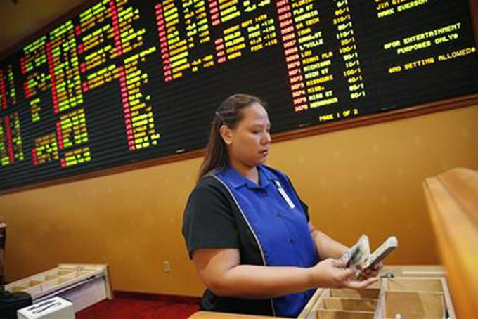 Therese Duenas counts money as she takes bets at in the sports book at the South Point hotel and casino Thursday, Aug. 20, 2015, in Las Vegas. On the board behind here are odds on NFL football and other bets. (AP Photo/John Locher)