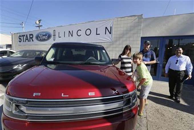 In this Thursday, July 2, 2015, photo, Robert Schemer, his wife, Kelly, and their son Graham, 9, pose next to their newly purchased pre-owned 2013 Ford Flex Limited, at the Star Ford Lincoln dealership in Glendale, Calif. At right is sales consultant Allan Calix. Summer deals and big demand for SUVs and luxury vehicles kept U.S. auto sales strong in July, according to reports released, Monday, Aug. 3, 2015. (AP Photo/Damian Dovarganes)
