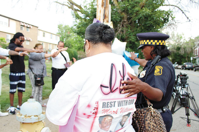 PRAYER VIGIL—Tamara Williams held a prayer vigil, July 31, to seek justice for her murdered brother Mark “Bizz” Williams. Mark Williams was murdered last year on July 31. The murderer still has not been found and no witnesses have come forward. The event was held on the corner of Bennett St. and Sterrett St. in Homewood. Photos: the shirts everyone was wearing.  Mark Williams sister Tamara Williams stands next to the pole with balloons and photographs of her brother. Police officer Tenisha Pettus stands with family and friends during prayer as they pray for all the family and justice for mark Williams. (Photos by J.L. Martello)