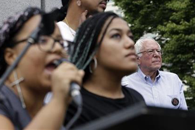 FILE - In this Aug. 8, 2015 file photo, Democratic presidential candidate Sen. Bernie Sanders, I-Vt. listens at right as Marissa Johnson speaks at left, accompanied by Mara Jacqueline Willaford, as the two women take over the microphone at a rally in downtown Seattle. The women, co-founders of the Seattle chapter of Black Lives Matter, took over the microphone moments after Sanders began speaking and refused to relinquish it. Sanders eventually left the stage without speaking further and instead waded into the crowd to greet supporters. Rising in political polls, Bernie Sanders is trying to overcome hurdles among black voters who are still learning about him and could help determine whether his insurgent campaign can last. (AP Photo/Elaine Thompson, File)