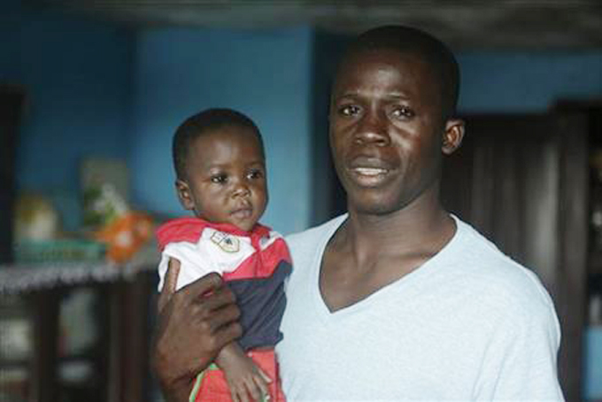 In this photo taken Tuesday, Aug. 18, 2015, nurse Donnell Tholley, 25, holds his adopted son Donnell Junior at their apartment in Freetown, Sierra Leone, as the baby’s great-grandmother Marie looks on. Tholley adopted the boy following the death of the mother Fatu Turay last year from the Ebola virus at the hospital on the outskirts of Freetown, Sierra Leone. The Ebola epidemic killed nearly 4,000 Sierra Leoneans and left thousands of orphans. (AP Photo/Sunday Alamba)