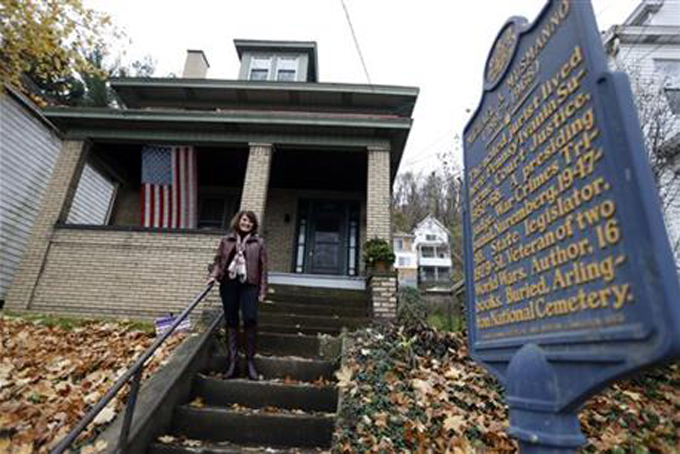 In this Wednesday, Nov. 11, 2015, photo, Patricia M. Homer stands on the steps of her home beside an historical plaque that marks the location of the home of former Pennsylvania Supreme Court Justice Michael A. Musmanno in McKees Rocks, Pa. Homer is the great-niece of Musmanno. Musmanno was a Navy attorney who presided at one of the Nuremburg war crimes trials. He re-interviewed various bunker witnesses on camera in 1948 to prove that Hitler was dead. A documentary called “The Day Hitler Died” will be shown on the Smithsonian Channel. The broadcast marks the first time viewers outside Germany will see a broadcast of interviews by Musmanno. (AP Photo/Keith Srakocic)