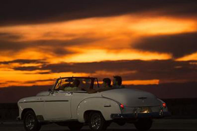 In this Sept. 30, 2015 file photo, tourists ride a vintage American convertible during sunset on the Malecon in Havana, Cuba. Tourism to Cuba has surged in the wake of improved relations with the U.S. (AP Photo/Desmond Boylan, File)