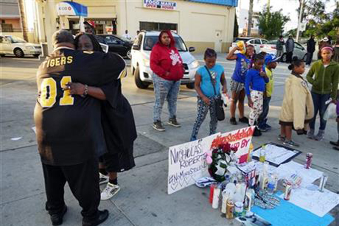 Latrice Barkus, Nicholas Robertson's aunt, facing camera, is embraced in front of the sidewalk memorial set up to honor her nephew on Sunday, Dec. 13, 2015, in Lynwood, Calif. Robertson was fatally shot Saturday by Los Angeles County Sheriff's deputies in Lynwood, south of Los Angeles. Authorities said Robertson was shot after he refused to drop a gun he was carrying. (AP Photo/David Martin)