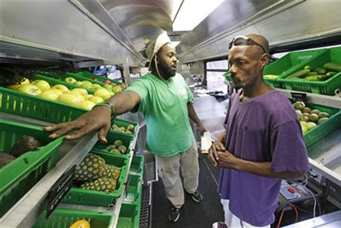 In this Wednesday, July 15, 2015 photo, Fresh Stop employee Jamar Allen, left, helps Jock Riggins as he shops on the Fresh Stop bus, a mobile market, in Eatonville, Fla.  (AP Photo/John Raoux) 