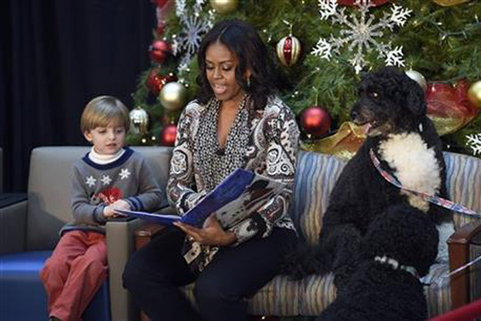 First lady Michelle Obama, sitting with Stephen Orzechowski, 5, left, and Bo Obama, right, reads "Twas the Night Before Christmas" to a group of children at the Children’s National Health System in Washington, Monday, Dec. 14, 2015. Her appearance continued a first lady tradition that dates back more than 60 years to Bess Truman, who first brought holiday cheer to children not well enough to leave the hospital in time for Christmas. (AP Photo/Susan Walsh)