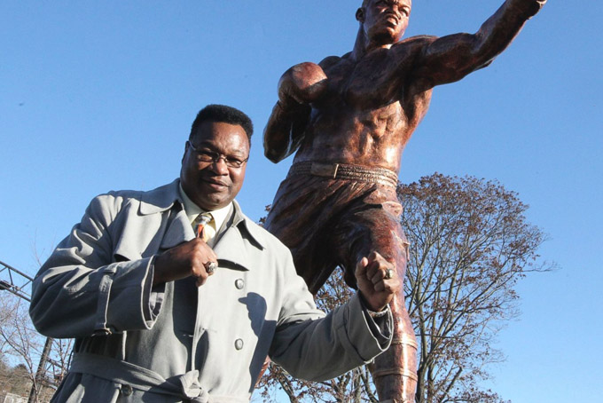 In this photo taken Monday, Dec. 7, 2015, Hall of Fame boxer Larry Holmes poses by a statue of his likeness as construction crews complete the installation of the new statue at Scott Park, where the Lehigh river runs into the Delaware in Easton, Pa. A dedication of the statue will take place Sunday, Dec. 13. (Sue Beyer/The Express-Times via AP)