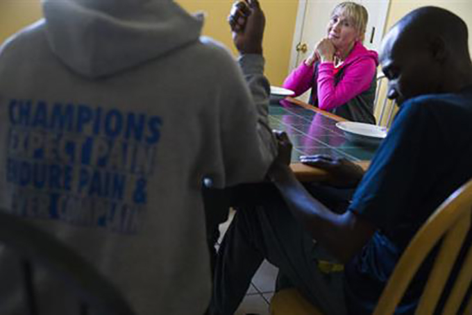 In this Saturday, Feb. 27, 2016, photo, race agent Larisa Mikhaylova sits with her runners, including Peter Kemboi, right, after being interviewed at the house where she boards her group in Newport, Ky. The International Association of Athletics Federations, working with the U.S. Anti-Doping Agency, is investigating multiple groups of athletes and agents based in the United States and Mexico, including Mikhaylova's that has won tens of thousands of dollars from races across the American Midwest but also become notorious for a rash of doping positives. (AP Photo/John Minchillo)