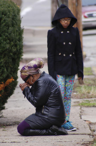 Carla Brown, left, prays as her daughter stands by in front of a house, Friday, March 11, 2016, where a shooting at a backyard party killed and wounded multiple people in Wilkinsburg, Pa. on Wednesday night. Brown said she was a close friend of the family that was attacked. (AP Photo/Keith Srakocic)
