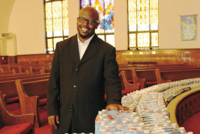 DONATIONS TO FLINT—St. James AME Church, in East Liberty, recently collected and sent hundreds of cases of bottled water to Flint, Mich., to help that community in its water crisis. Pictured above, Rev. Rodrecus Johnson Jr., the senior pastor who organized the water drive, stands with some of the donated water. (Photo by J.L. Martello)