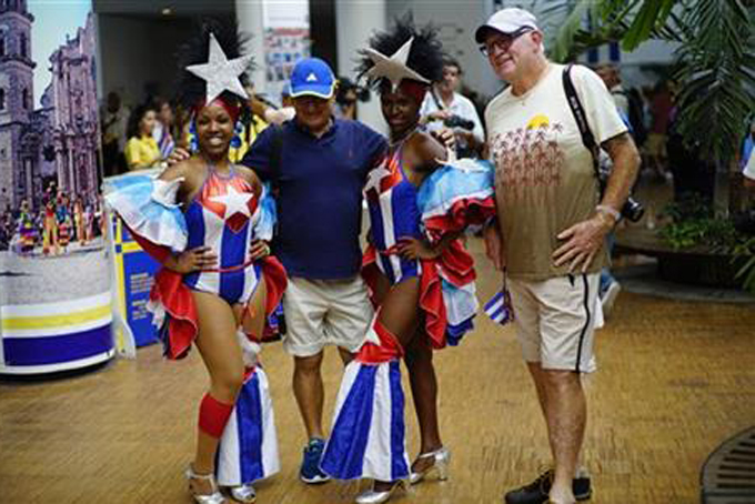 FILE - In this May 2, 2016 file photo, passengers from Carnival's Adonia cruise ship pose with Cuban dancers upon arrival from Miami, in Havana, Cuba. Around the world, television viewers watched prosperous-looking Americans greeted by trays of rum drinks and Afro-Cuban dancers in skimpy Cuban flag-patterned bathing suits. For many Cubans, it was a spectacle uniting the worst exotic stereotypes about their country with disrespect for a symbol of independence. (AP Photo/Ramon Espinosa, File)