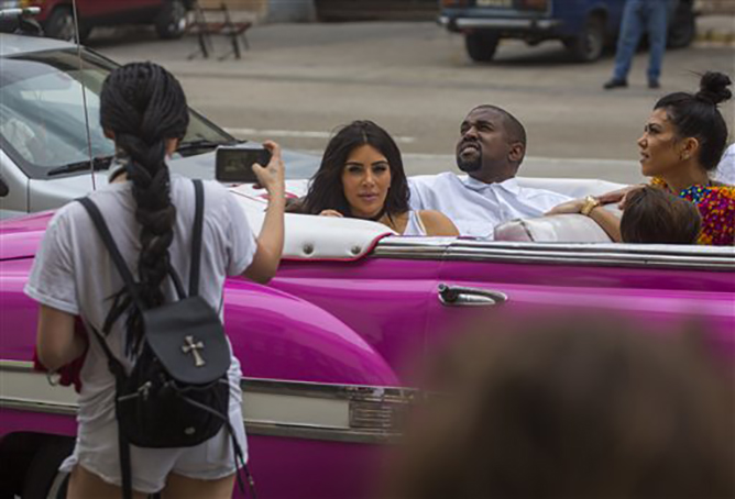 A woman uses her cellphone to take a picture of American reality-show star Kim Kardashian West, center, and her husband Kayne West as they ride on a classic car along the streets of Havana, Cuba, Wednesday, May 4, 2016. At right is Kourtney Mary Kardashian.(AP Photo/Desmond Boylan)