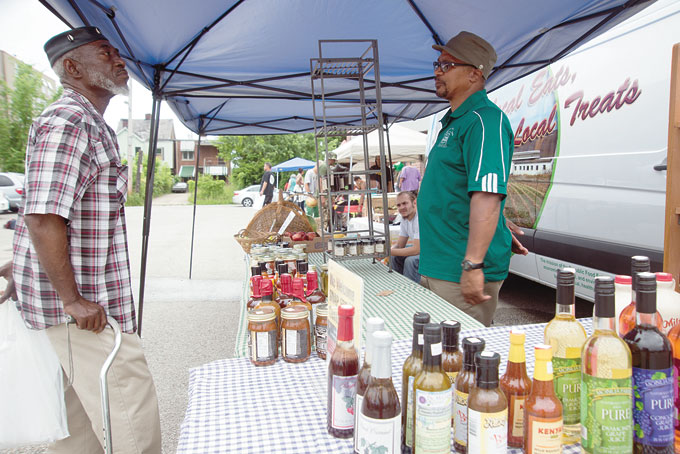 GRAND OPENING—Moses Bey, left, talks to William Peterson of Republic Food Enterprise during the grand opening of the Homewood Community Farmers Market. 